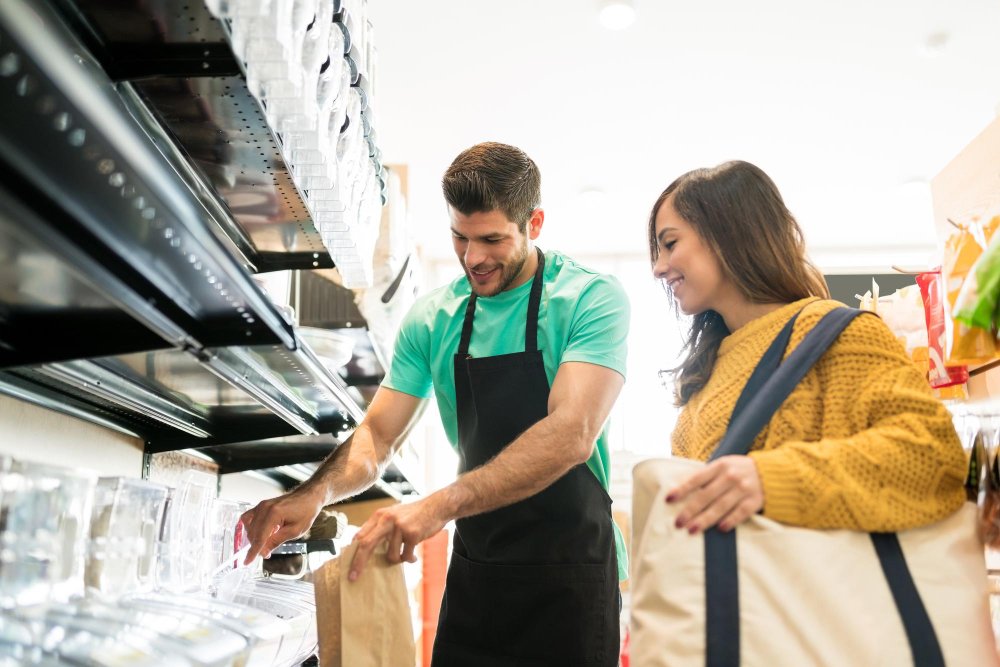 vendedor seguro de si mismo empacando alimentos para una mujer en una tienda de comestibles